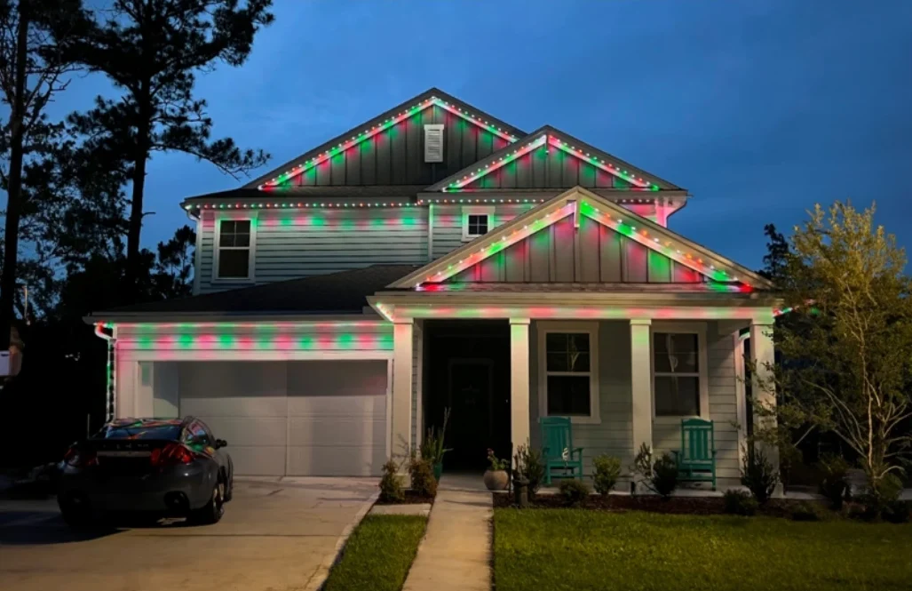 Red and green permanent lighting along the gables and porch of a home